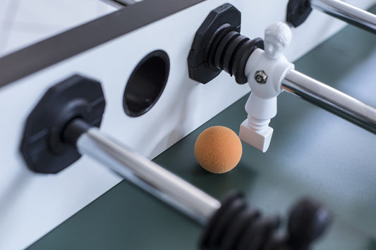 White Foosball player hitting an orange ball in game of Table Soccer